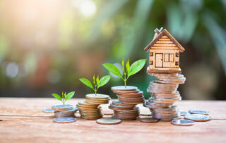 Stacks of coins with sprouts and a small house model sitting on top.